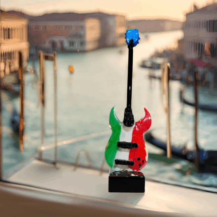 Una chitarra in miniatura realizzata a mano in Vetro di Murano. Poggia su una solida base quadrata in vetro nero e sul corpo della chitarra brilla il tricolore italiano