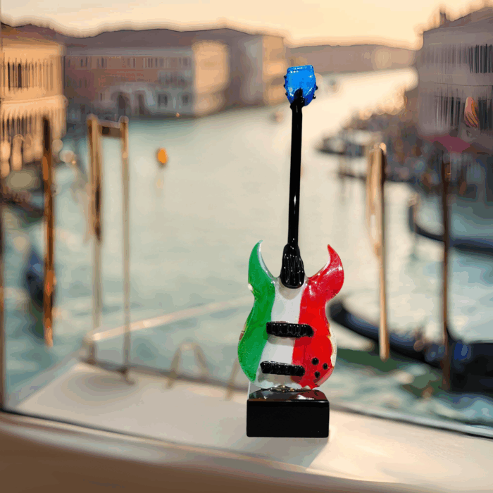 Una chitarra in miniatura realizzata a mano in Vetro di Murano. Poggia su una solida base quadrata in vetro nero e sul corpo della chitarra brilla il tricolore italiano