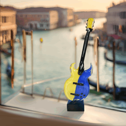 Originale chitarra realizzata a mano con la tradizionale tecnica a lume muranese. Decorata in due colori color-block intensi e contrastanti, il giallo e il blu. Poggia su una base quadrata in vetro nero.